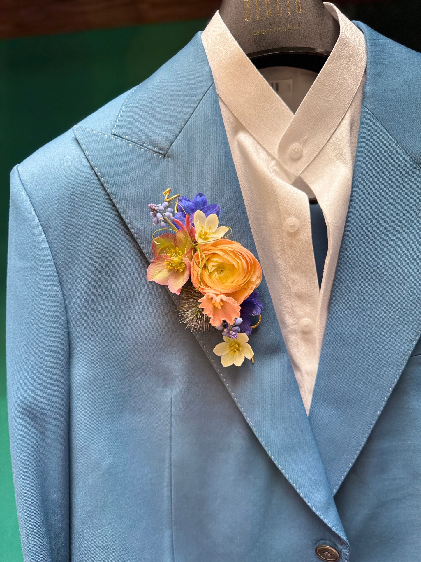 Blue suit jacket with an artful, colorful floral boutonniere with a peach ranunculus.