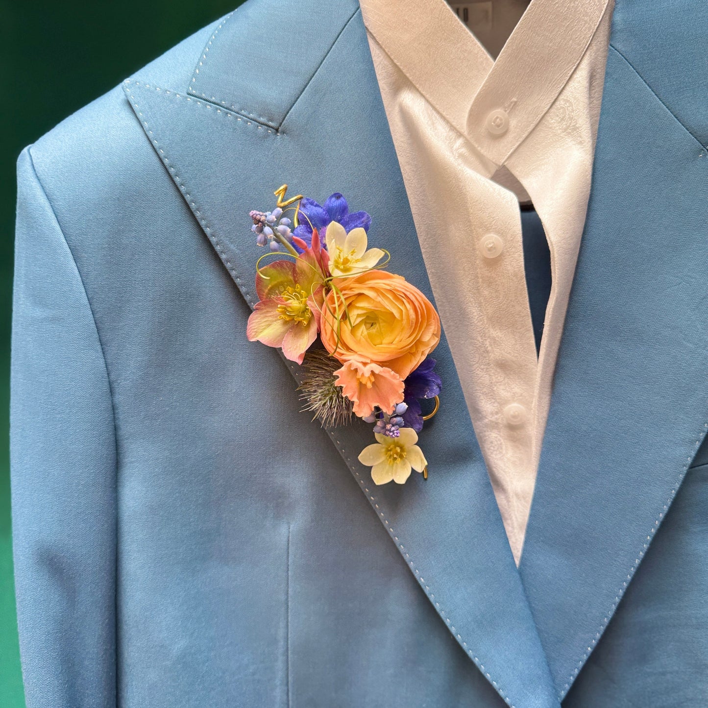 Peach ranunculus and helleborus lapel piece with a pop of periwinkle, blue and butter yellow