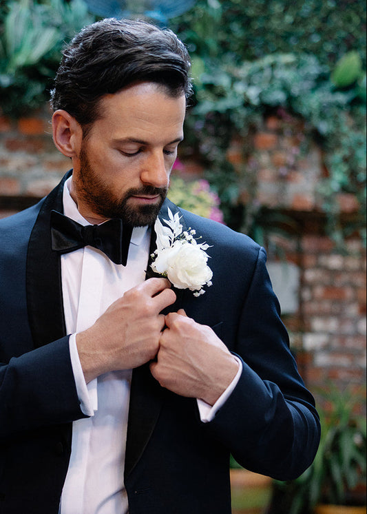 Man in a black tuxedo adjusting an all white boutonniere with no greenery.