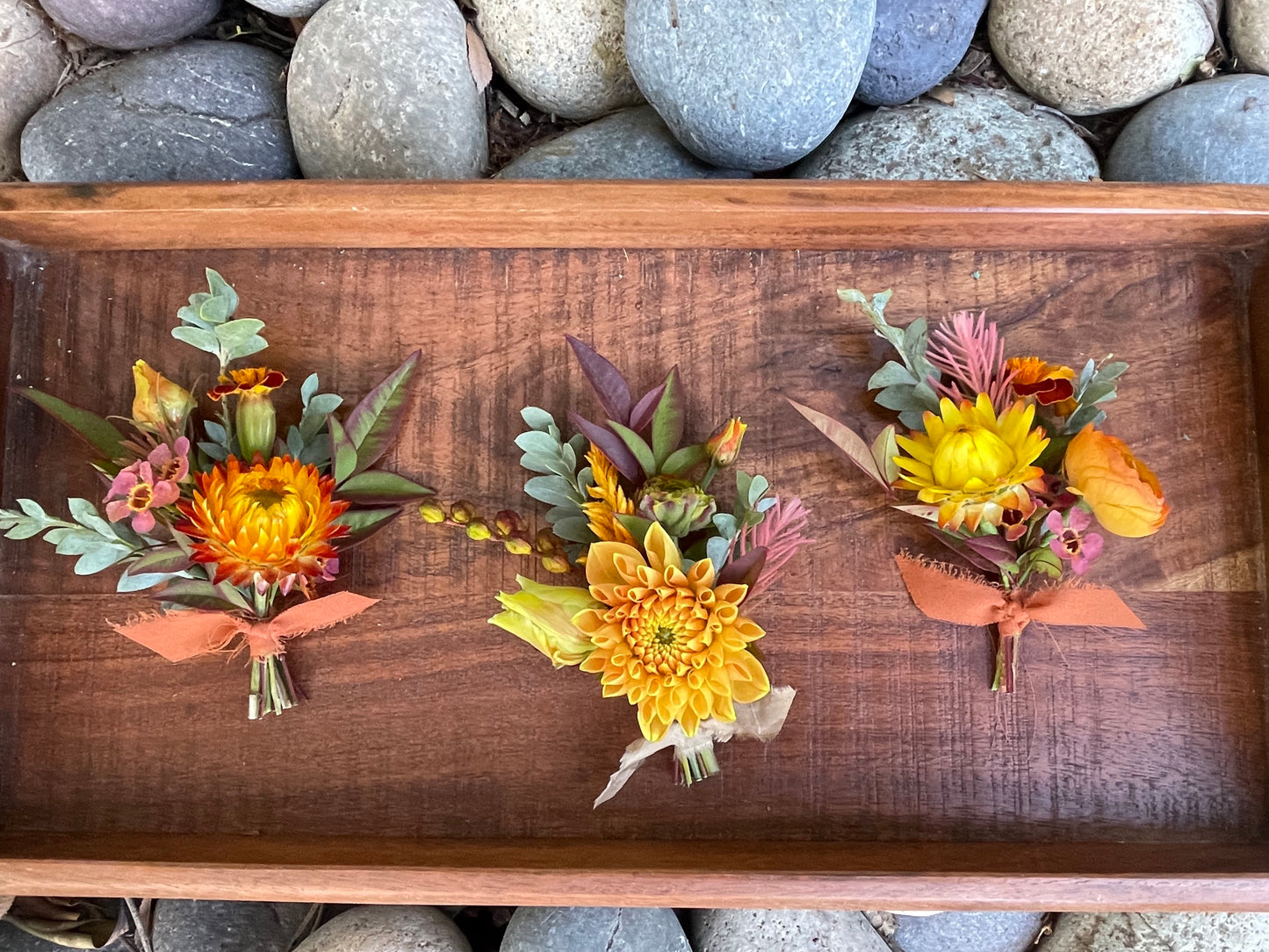 Three Fall standard boutonnieres tied with ribbon on a wooden tray.