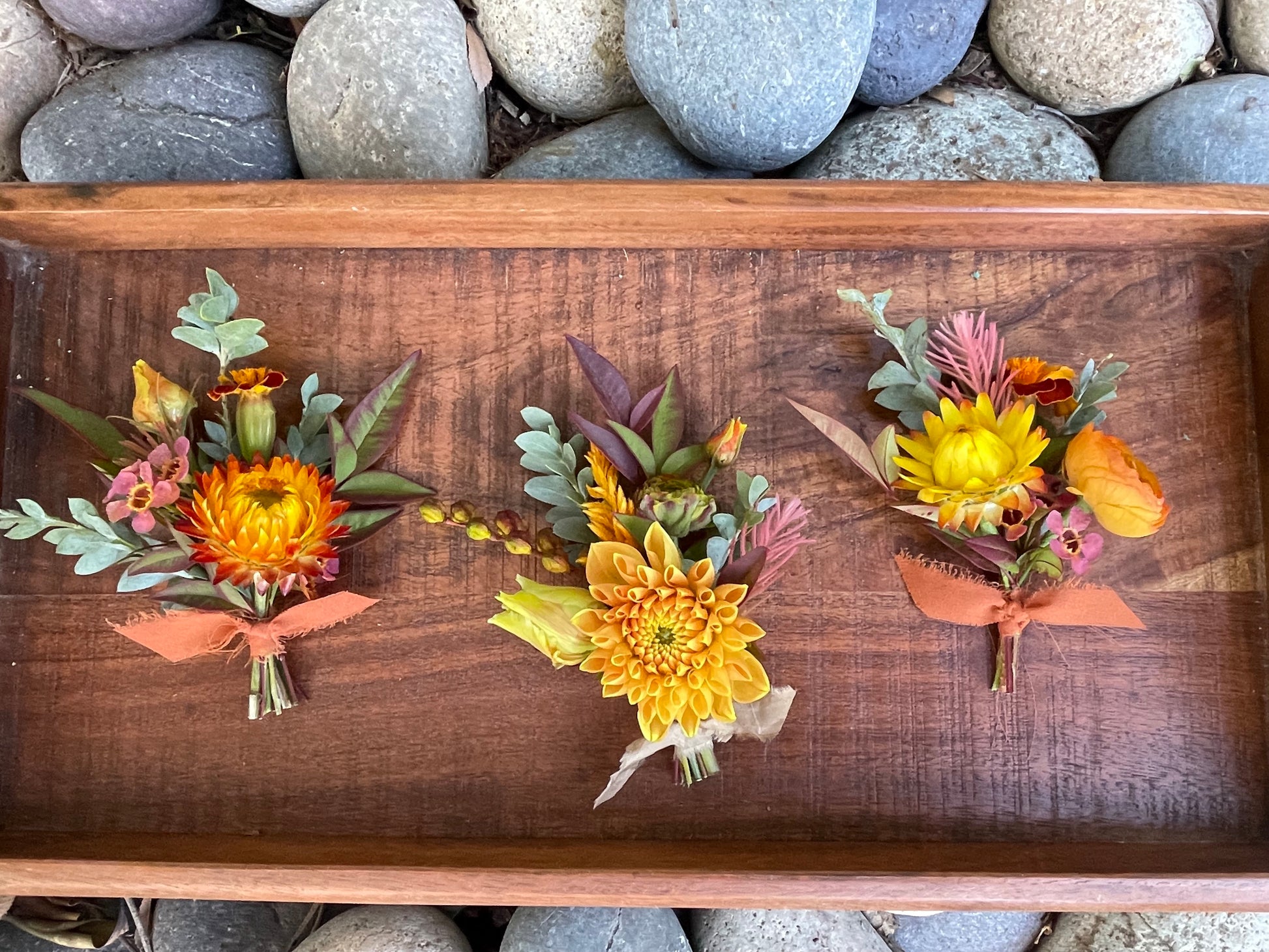 Three Fall standard boutonnieres tied with ribbon on a wooden tray.