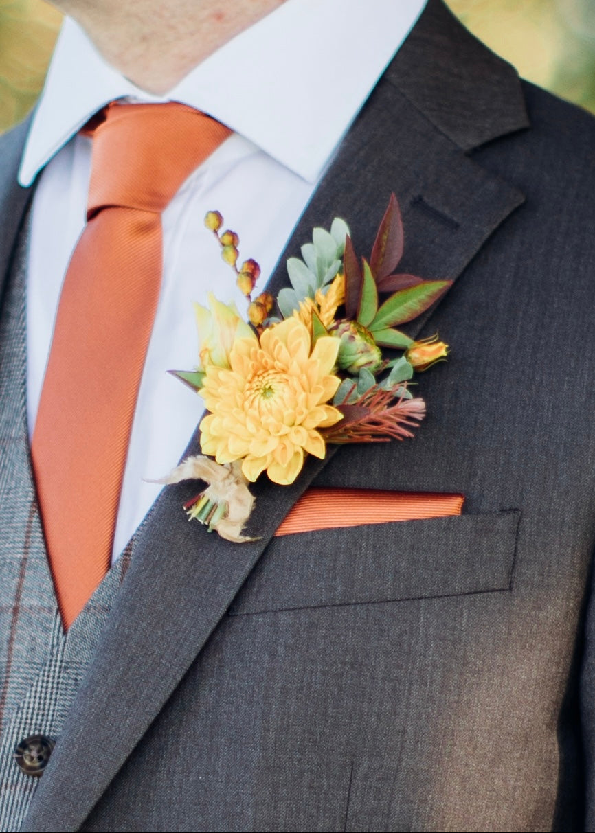 Gray suit with yellow floral boutonniere and orange tie