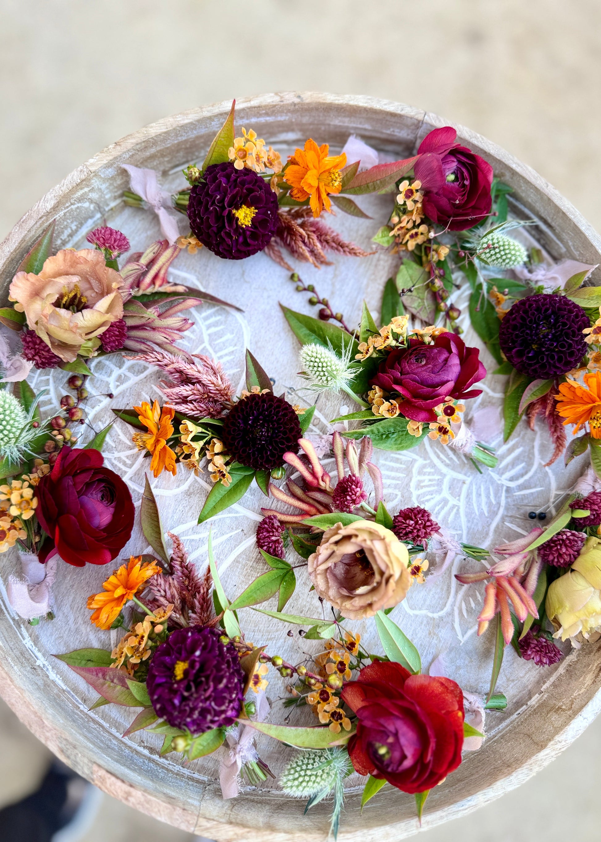 Colorful Boutonnieres with pops of burgundy, orange and tan fall tones laid on a circular tray.