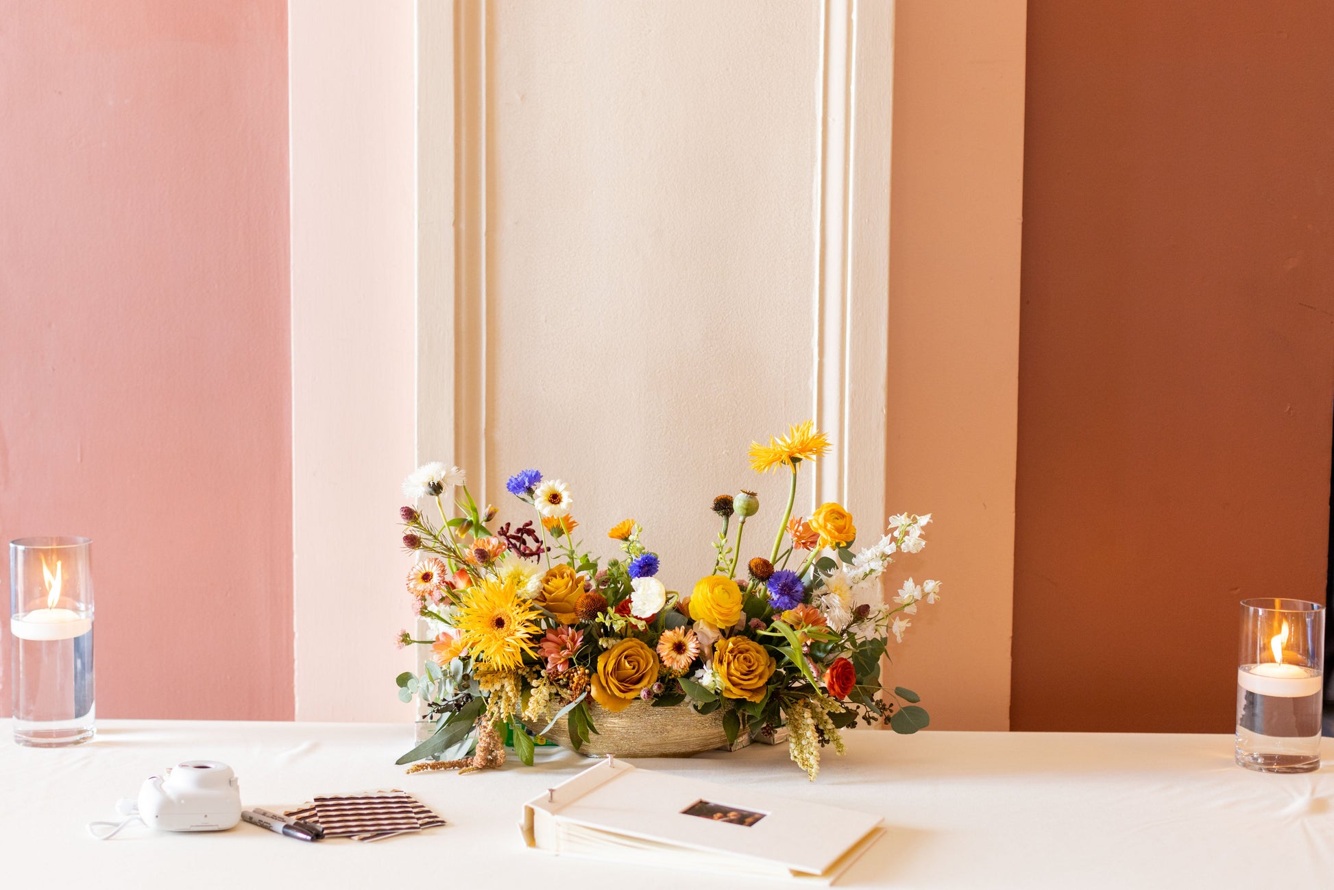 Long Floral Arrangement with gold, cream, yellow, terracotta and blue flowers on a welcome table at a wedding with floating candles.