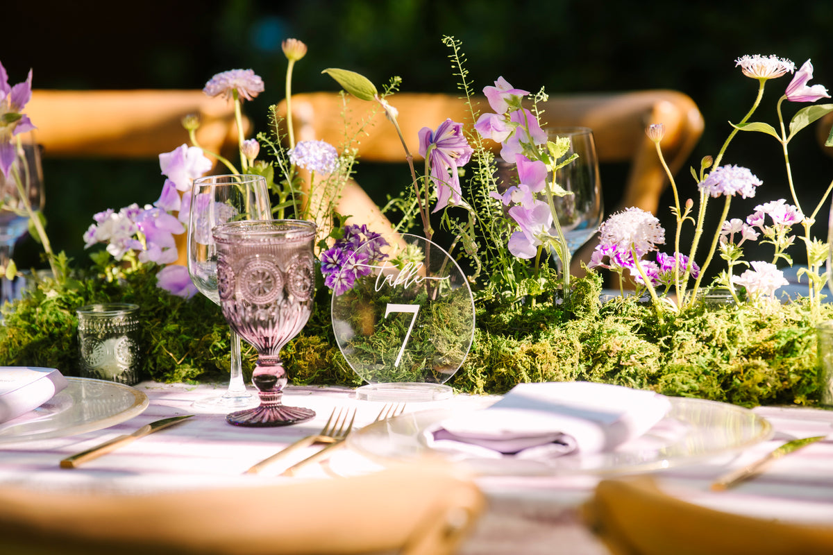 An organic, mossy long centerpiece featuring lavender flowers made to look like it is growing out of the long farm table.