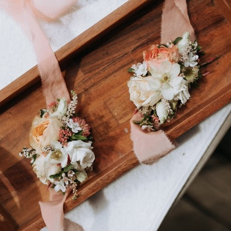 two blush peach and white ribbon wrist corsages on a wood tray