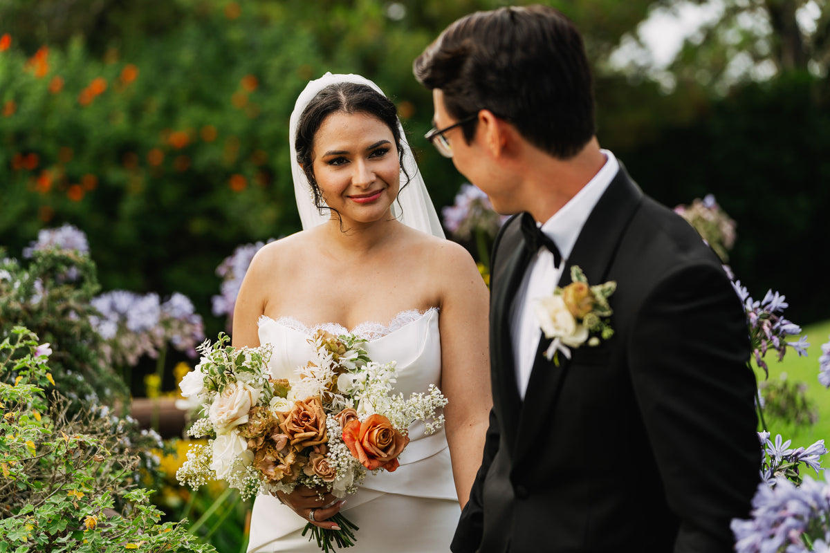 A bride holding a bouquet of neutral toned, beige, gold, tan, cream and white flowers with babies breath and garden roses.