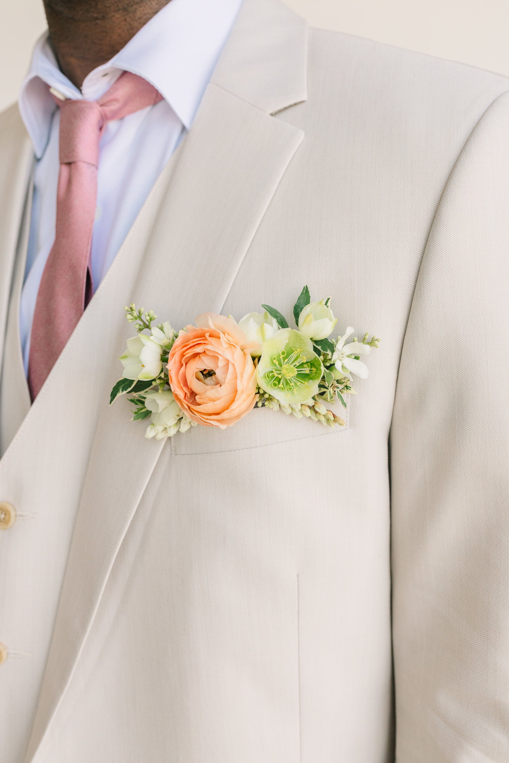 Peach Ranunculus pocket square boutonniere on a light gray suit jacket with a pink tie.