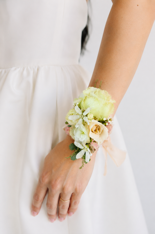 Floral wrist corsage on a person wearing a white dress tied with a silk ribbon