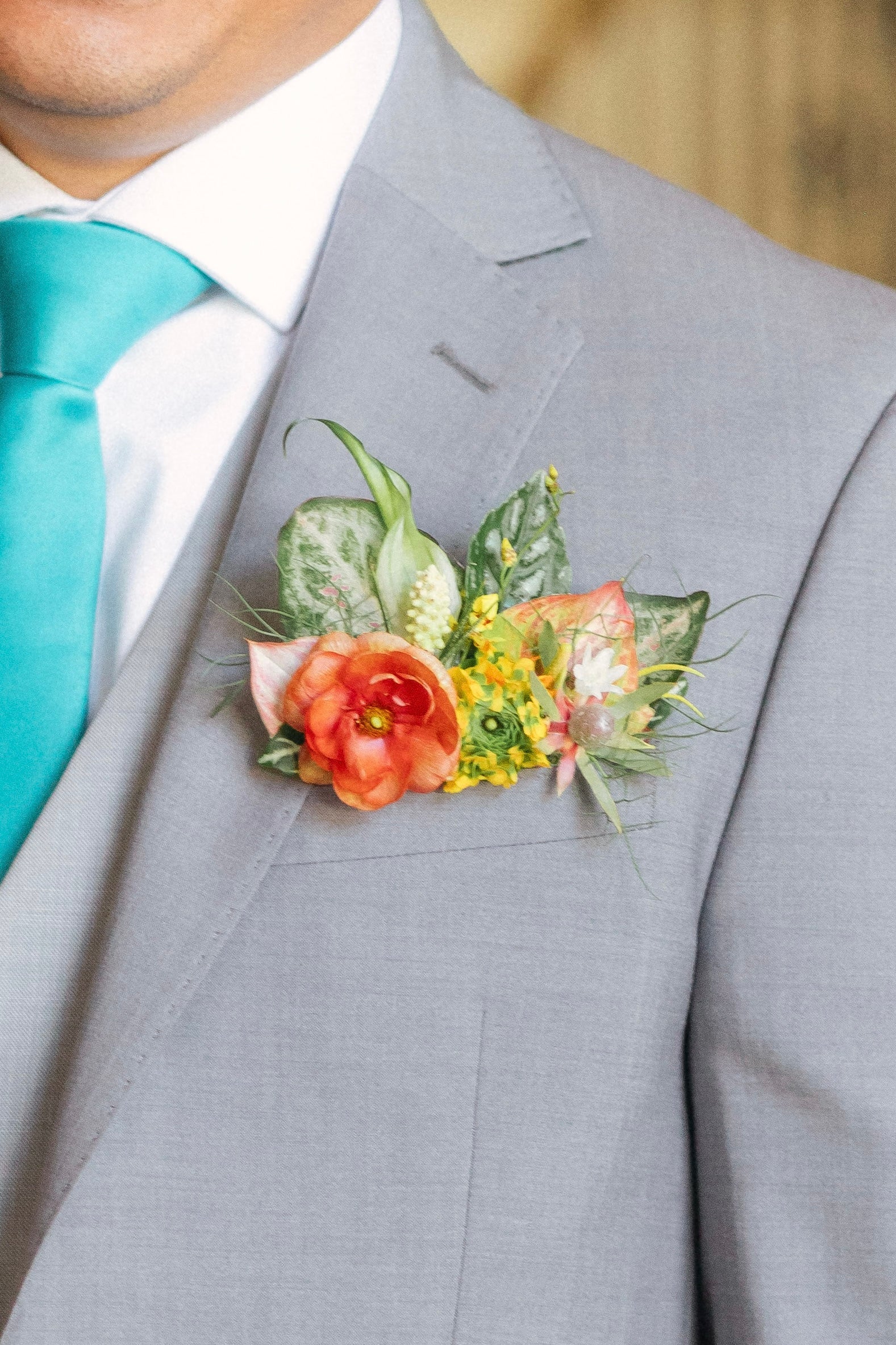 A tropical pocket square boutonniere on a gray suit with a turquoise tie