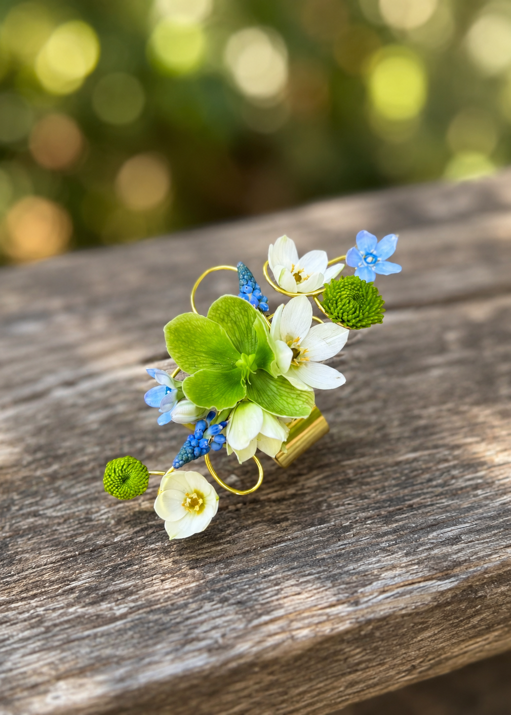 A beautiful and artful gold metal cuff wristlet corsage with green, white, and blue flowers.