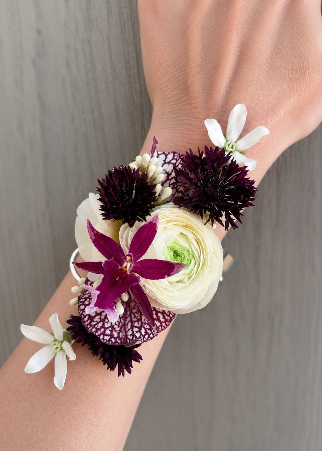Floral wrist corsage with Burgundy and white flowers on a wrist.