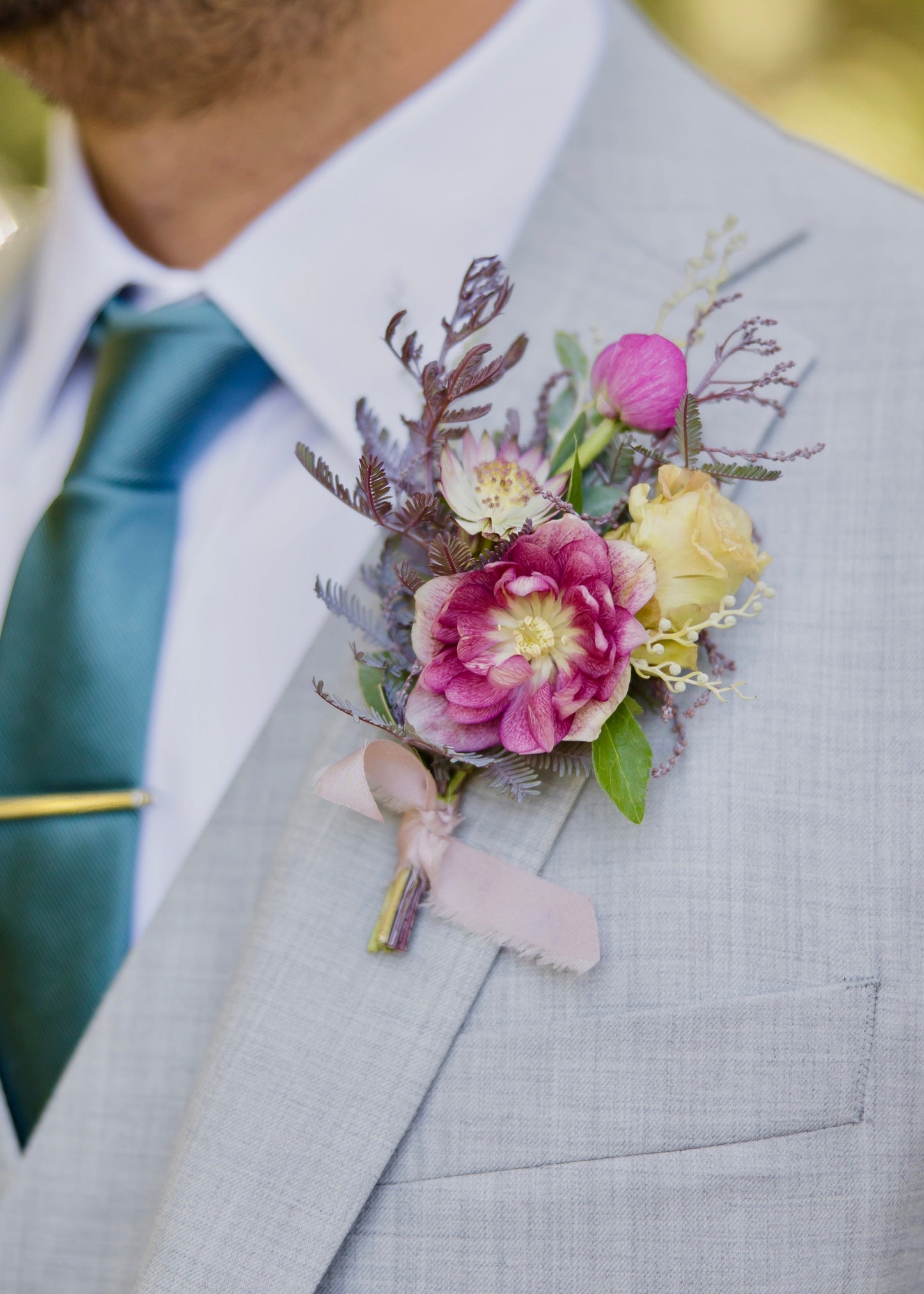 Man wearing a gray suit with a wildflower boutonniere and green tie.
