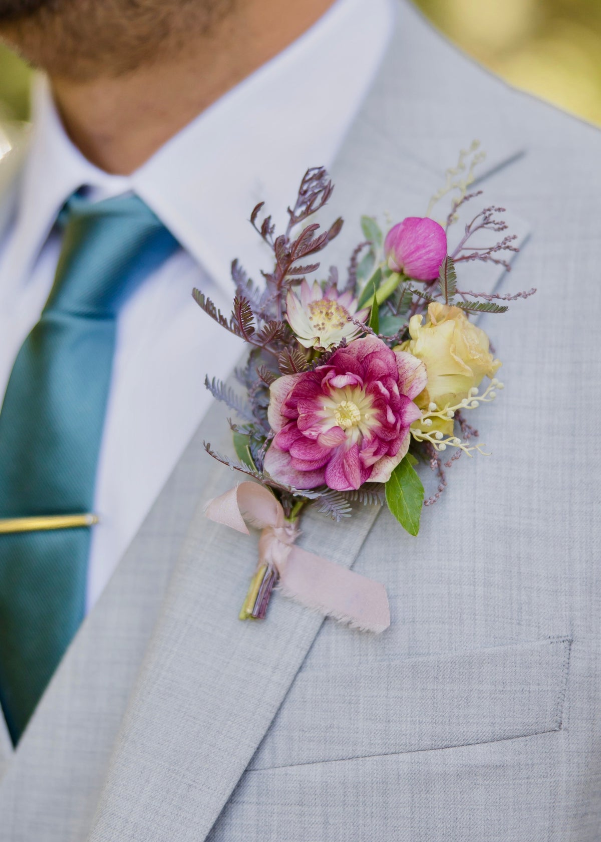 Man wearing a gray suit with a wildflower boutonniere and green tie.