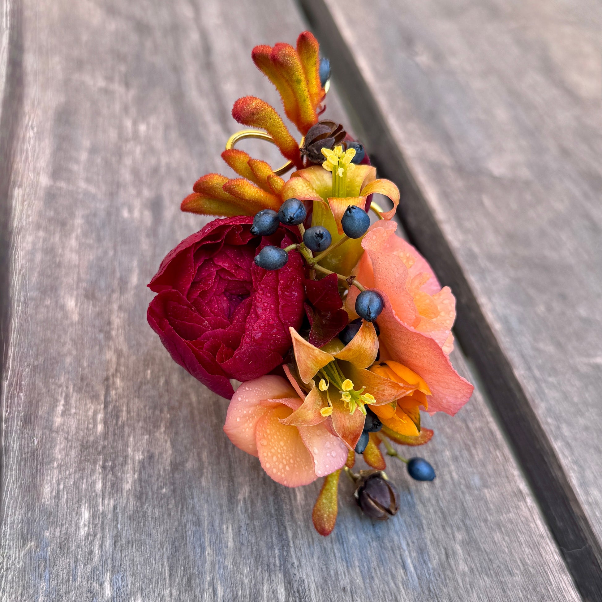 Colorful wrist corsage with red ranunculus, orange, and peach flowers with pops of navy blue